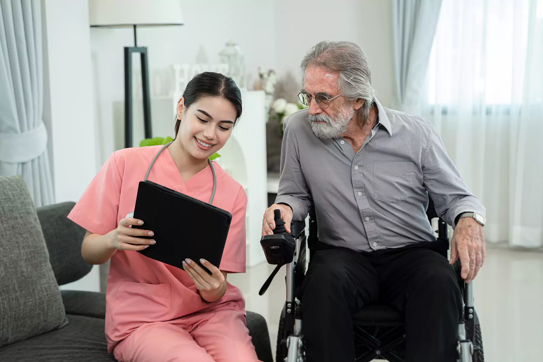 A nurse and a disabled old man sitting in his wheelchair looking at the tablet